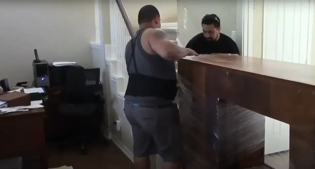 Two movers carrying a wooden desk out of an office